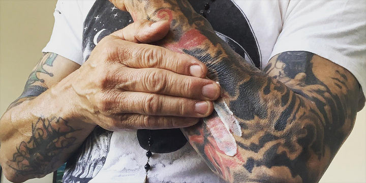 man is applying ointment to the tattoos on his left arm